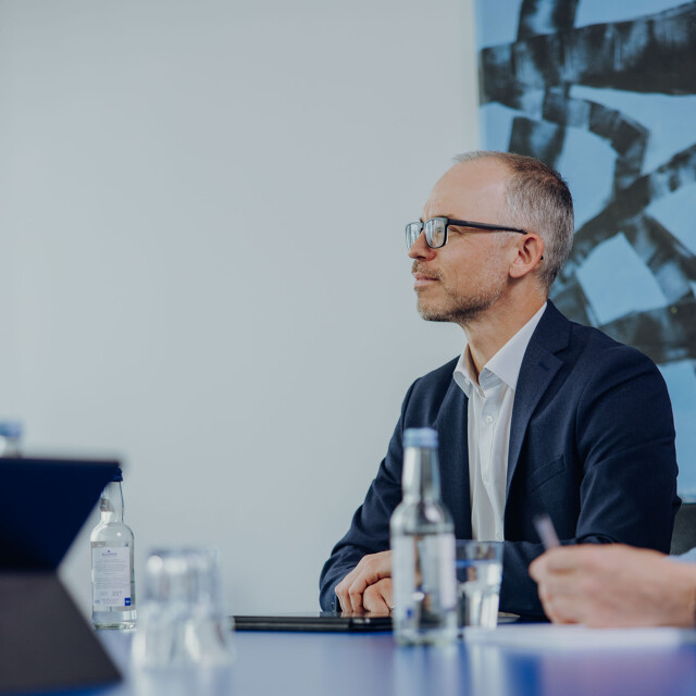 Roland Gruber Eine Person sitzt am Besprechungstisch der ATG und unterhält sich mit Kollegen